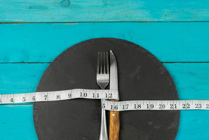 fork and knife constricted by measurement tape depicting an eating disorder