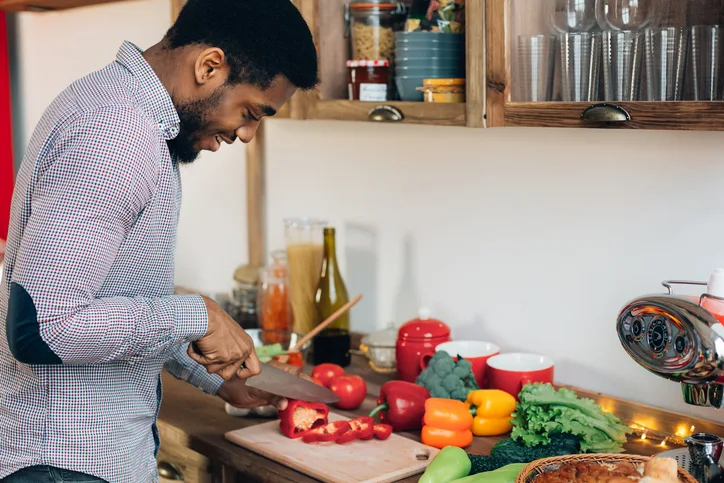 African-american man preparing delicious and healthy food in kitchen, cutting fresh vegetables, copy space