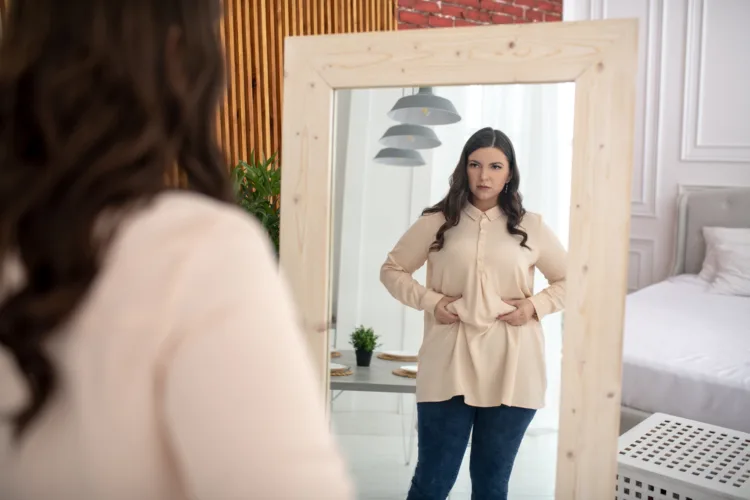 Need to keep a diet. Young woman in a beige blouse touching her belly