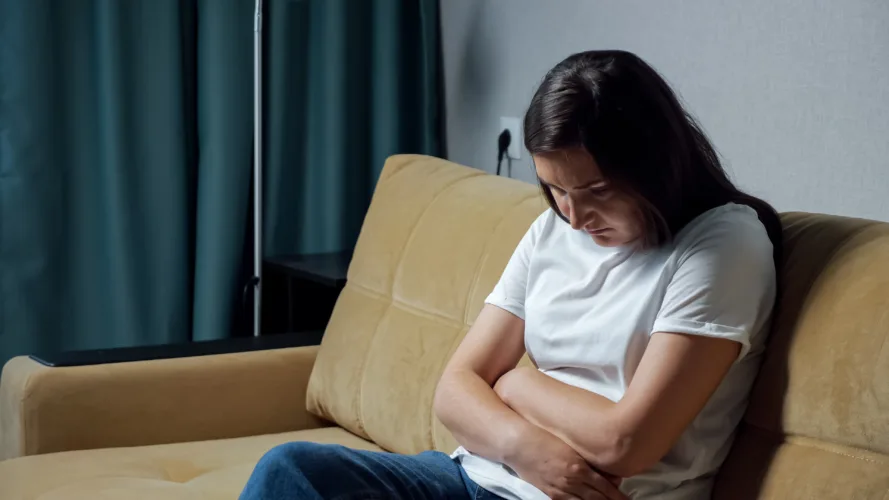 Young woman hunched over holding belly while sitting on the couch.